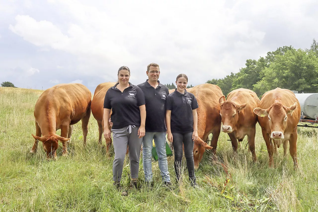 Rolnicza rodzina Kohlmannów stoi na pastwisku z bydłem limousine w tle