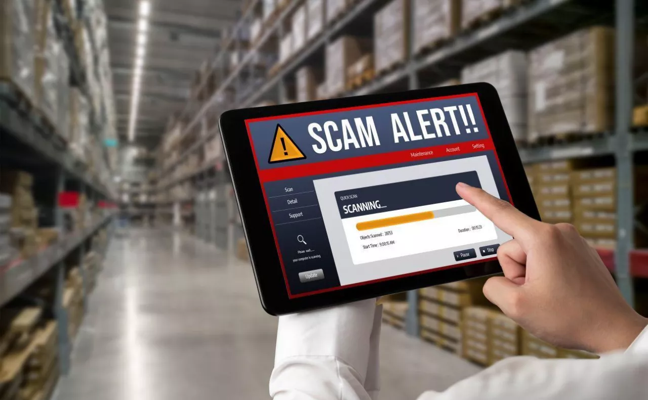 Tablet z komunikatem ostrzegawczym podczas analizy danych w magazynie logistycznym. Grafika symbolizuje cyfrowe systemy wykorzystywane do monitorowania transportów żywności i wykrywania nieprawidłowości w handlu.