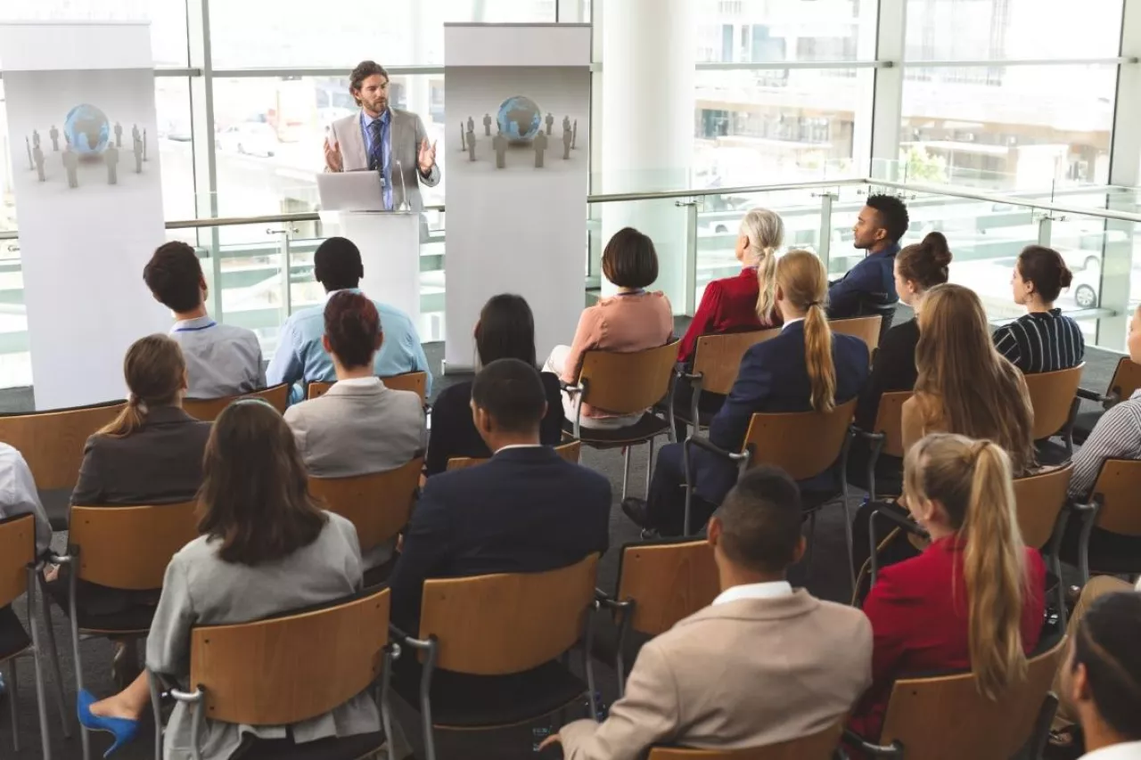 High angle view of Caucasian male speaker with laptop in front of diverse group of business people sitting at business seminar in office building