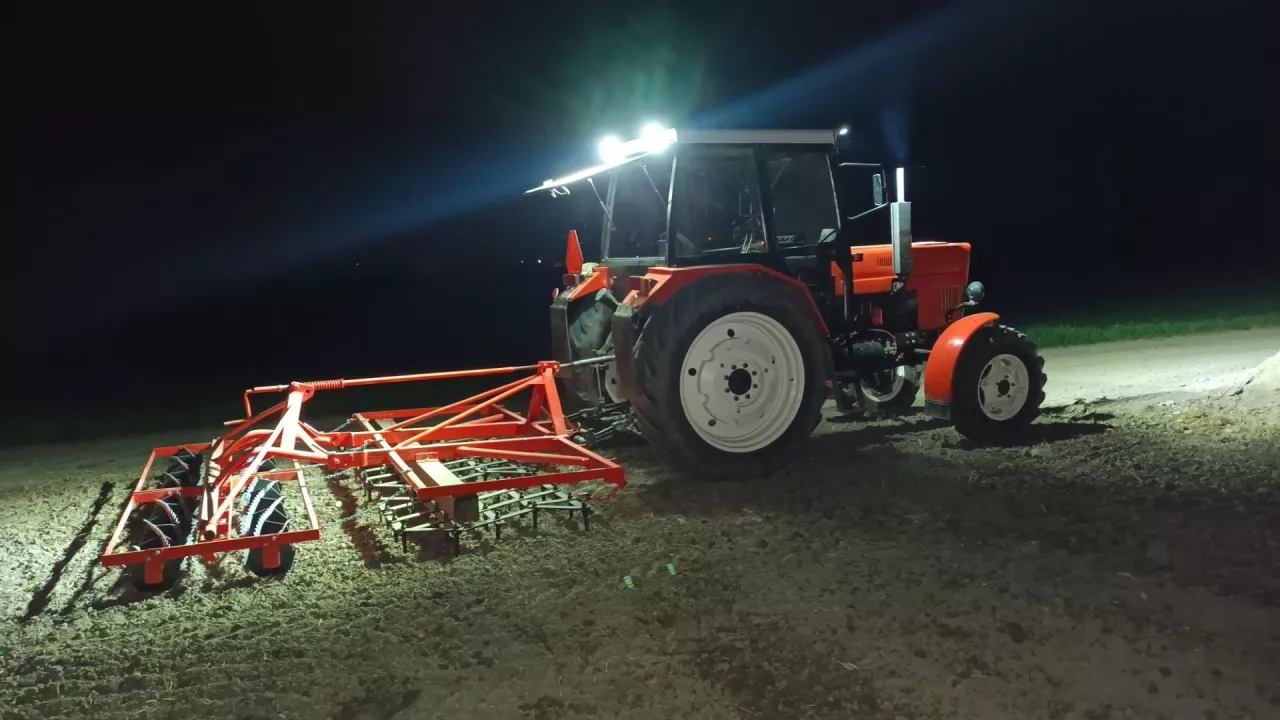 Ciągnik MTZ-82 z zaczepionym agregatem uprawowym podczas pracy na polu w nocy